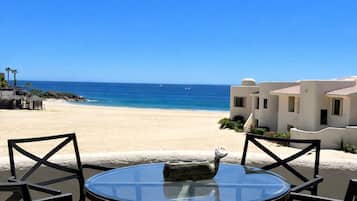 A round glass table with four chairs, a stone sculpture, and a view of a beach and ocean.