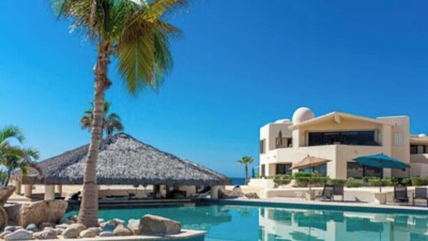 A resort with a swimming pool, palm trees, and a building with a thatched roof. - ALL NEW remodeled condo! Ocean Front on Beach 2 Bd 2 Ba Upper Level (Cabo San Lucas)