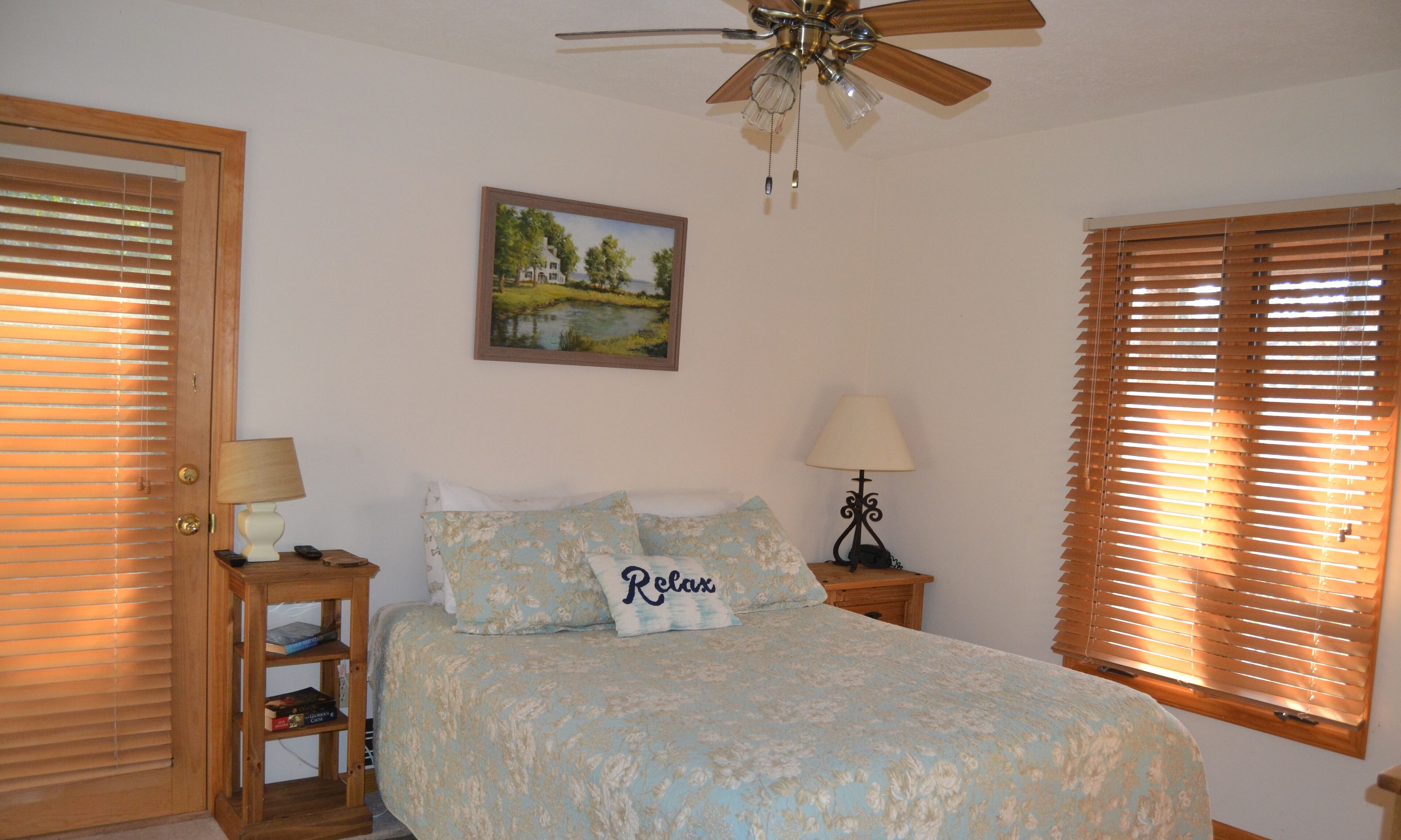 A bedroom with a bed, two bedside tables, a ceiling fan, and a painting on the wall.
