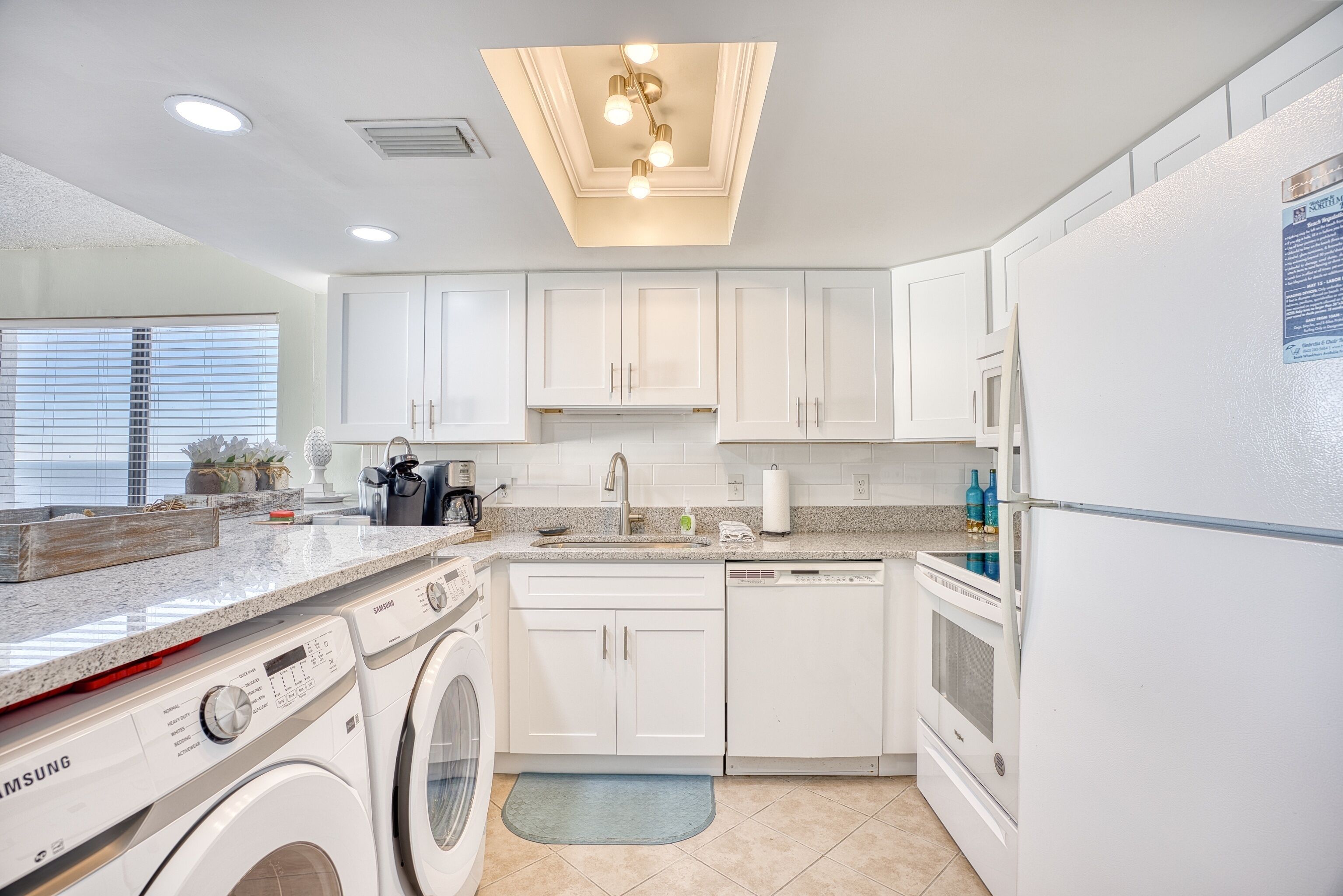 Une cuisine moderne avec des meubles blancs, un lave-linge, un lave-vaisselle et un réfrigérateur.