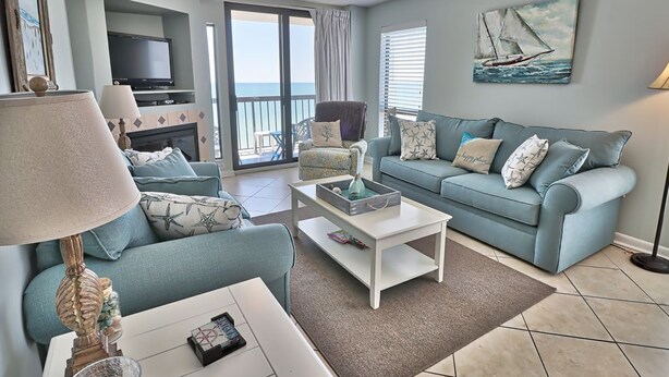 Un salon avec un canapé bleu, une table basse blanche et un téléviseur posé sur un meuble. On y trouve une cheminée, une lampe et un tableau représentant un voilier accroché au mur.