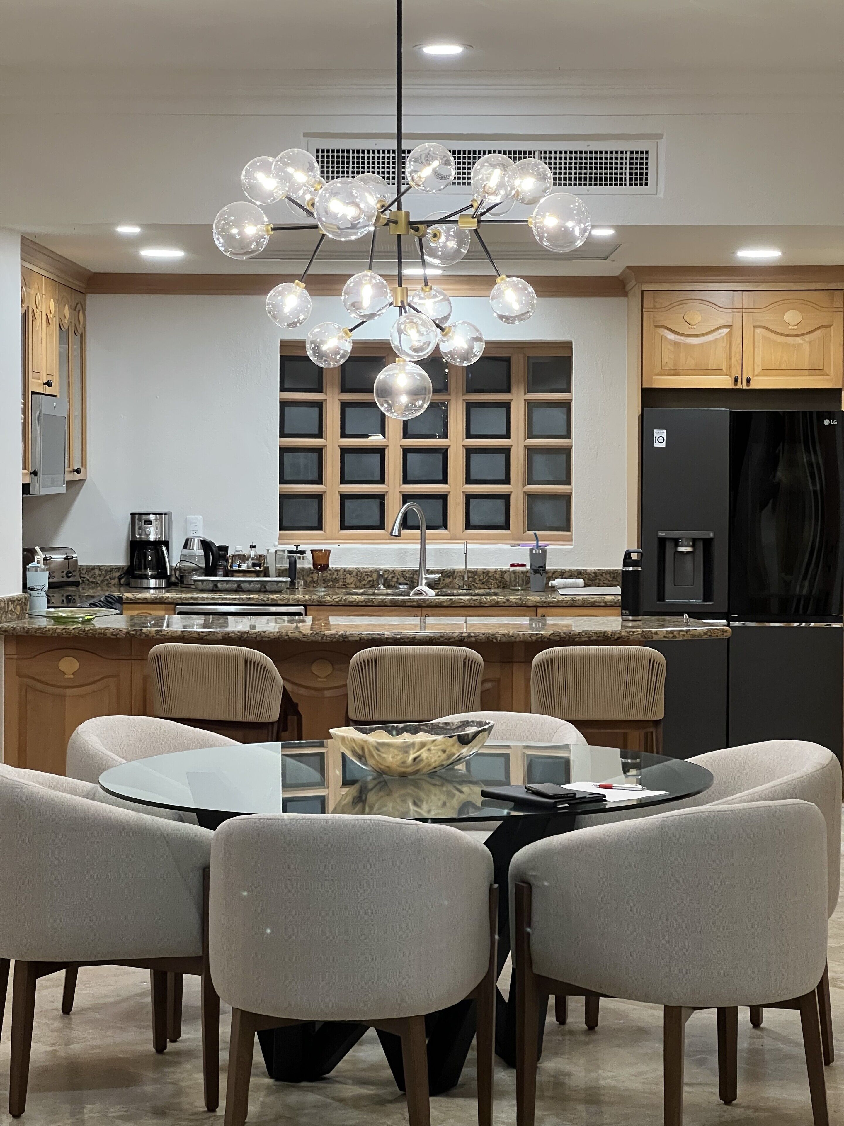 A modern kitchen with a central island, a dining table with chairs, and a unique spherical chandelier.