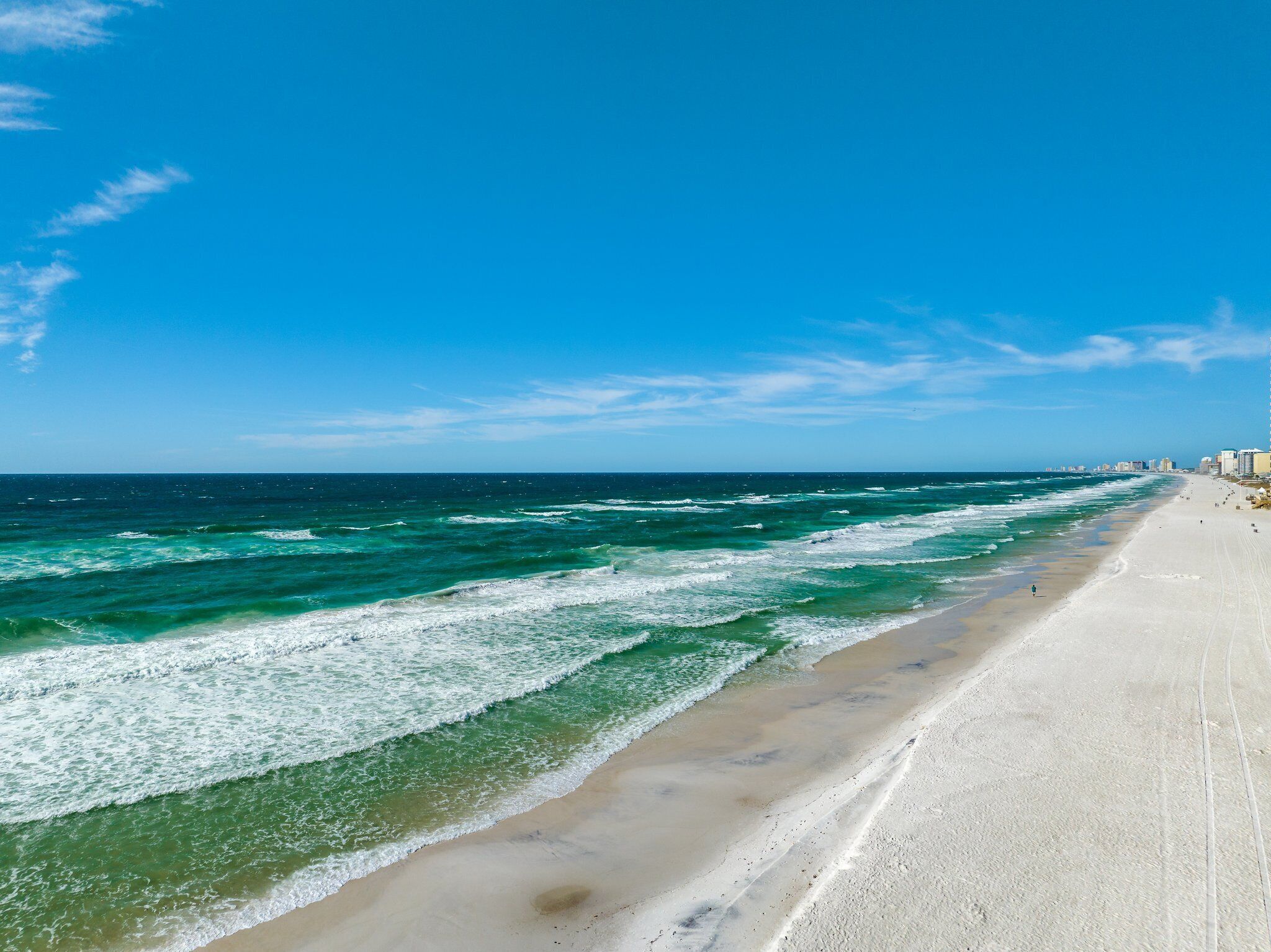 Een strand met golven, een heldere lucht en gebouwen in de verte.
