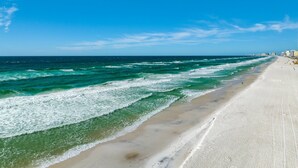 Ein Strand mit Wellen, blauem Himmel und Gebäuden in der Ferne.