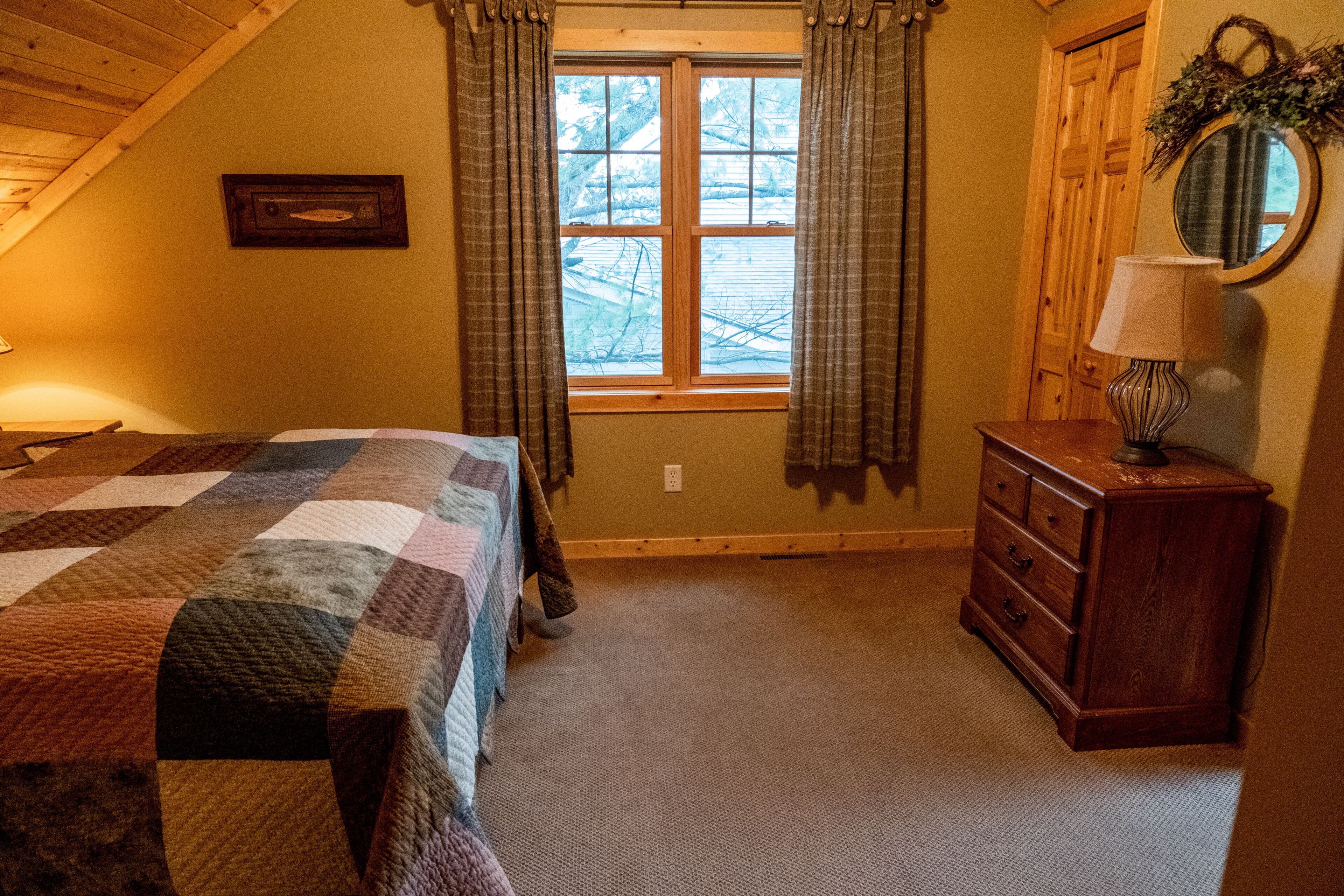 Een slaapkamer met een bed, een lakenkast, een raam met gordijnen en een spiegel aan de muur.