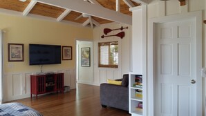 A living room with a wooden ceiling, a television, a red cabinet, a gray sofa, and a bookshelf. - Ocean Beach Home In The Heart Of Authentic Old Hawaii (Captain Cook)