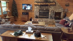 A cozy log cabin interior with a stone fireplace, a television mounted on the wall, and a comfortable seating area with a sofa and a coffee table. - Adventurewood Luxury Log Cabin - Hot Tub, Fireplace, Pool Table (Bloomington)