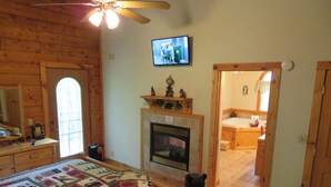 A cozy room with a fireplace, wooden walls, a quilt on the bed, and a television on the wall. - Adventurewood Luxury Log Cabin - Hot Tub, Fireplace, Pool Table (Bloomington)