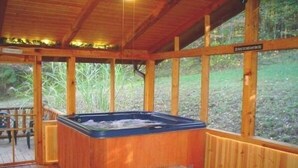 A wooden hot tub in a covered outdoor area with a wooden deck and a view of the surrounding greenery. - Adventurewood Luxury Log Cabin - Hot Tub, Fireplace, Pool Table (Bloomington)