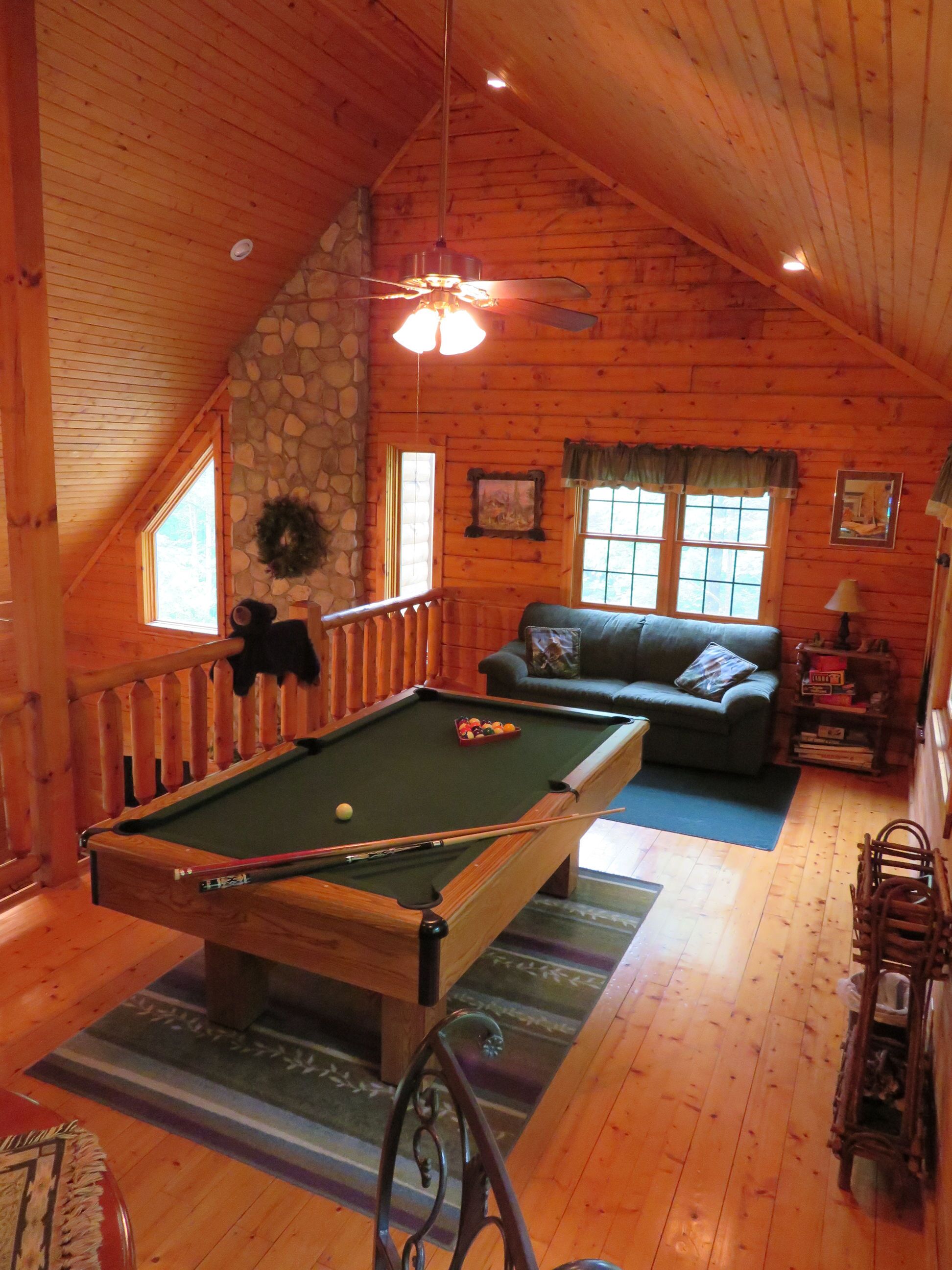 A cozy wooden cabin with a pool table, a sofa, and a stone wall.