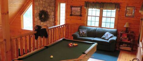 A cozy wooden cabin with a pool table, a sofa, and a stone wall.