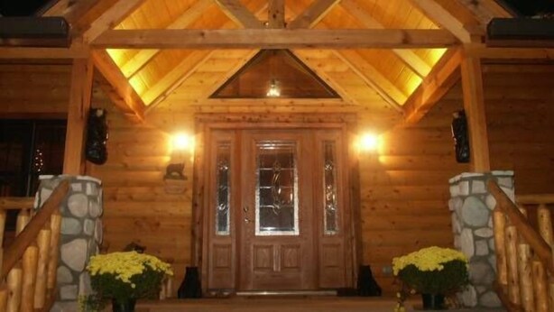 A wooden cabin with a pitched roof, stone pillars, and a front door with glass panels. - Adventurewood Luxury Log Cabin - Hot Tub, Fireplace, Pool Table (Bloomington)