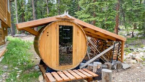 A wooden cabin with a circular door, a wooden deck, and a stone pathway. - Cedar Barrel Sauna & Mtn Views - Pet-Friendly, 20 mi to Breckenridge (Fairplay)