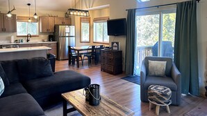 A modern kitchen with a central island, a dining area with a table and chairs, a living room with a sofa and a TV, and a large window with curtains. - Cedar Barrel Sauna & Mtn Views - Pet-Friendly, 20 mi to Breckenridge (Fairplay)