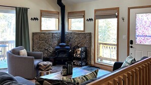 A cozy living room with a fireplace, a ceiling fan, and a stone wall. - Cedar Barrel Sauna & Mtn Views - Pet-Friendly, 20 mi to Breckenridge (Fairplay)