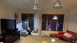 Una cocina moderna con lavavajillas integrado, encimera de granito y pileta de acero inoxidable. Hay un sofá rojo y una zona de comedor con mesa y sillas.