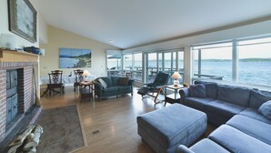 A spacious living room with a fireplace, a large sofa, and a view of the water.