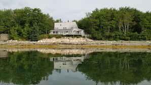 A house with a deck, surrounded by trees and a rocky shoreline.