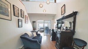 A spacious living room with a high ceiling, a dark blue sofa, a wooden coffee table, and a large ornate mirror.