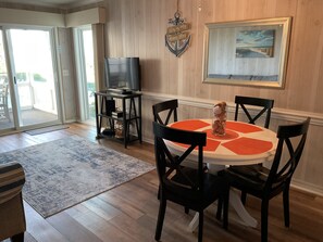 A dining area with a round table, black chairs, a television on a stand, a rug, and a framed picture on the wall.