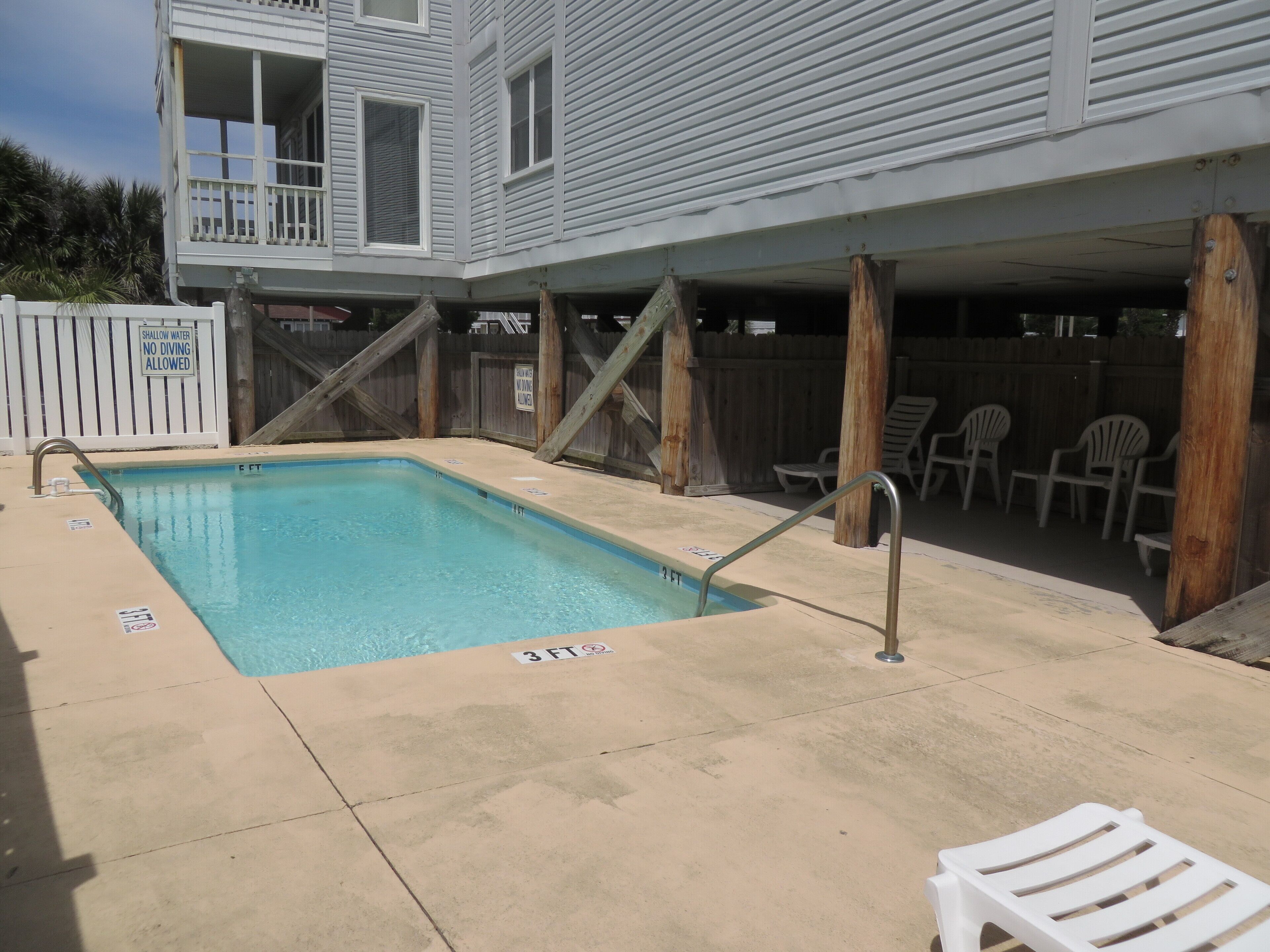 Une piscine rectangulaire dont la profondeur maximale est indiquée à 3 pieds, entourée d’une terrasse en béton et de chaises longues en bois.