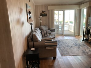 A living room with a sofa, a coffee table, a TV stand, and a sliding glass door leading to an outdoor area.