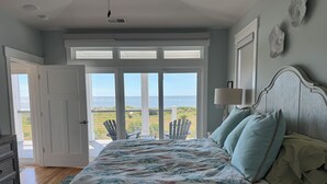 Ett sovrum med en stor säng, utsikt över havet och en dörr som leder ut till en balkong.