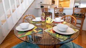 A dining area with a glass table, white plates, and wooden chairs. A bottle of wine and a fish-shaped decoration are on the table.