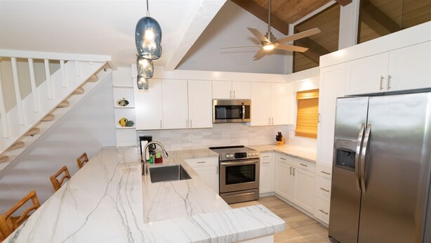 A modern kitchen with white cabinetry, a marble island, stainless steel appliances, and a ceiling fan.