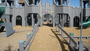 A playground with multiple play structures, including slides and climbing areas, surrounded by a wooden fence. - Magnificent Mountain Side~Recently Remodeled (Frisco)