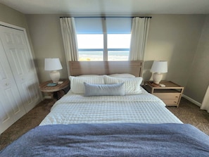 Una habitación de hotel con una cama, dos mesitas de noche y una vista a la playa.