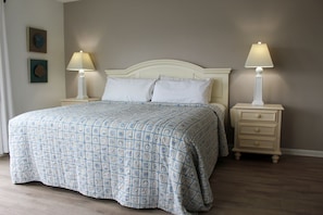 Una cama bien hecha con una colcha estampada, dos mesitas de noche con lámparas, y una pared con dos cuadros enmarcados.
