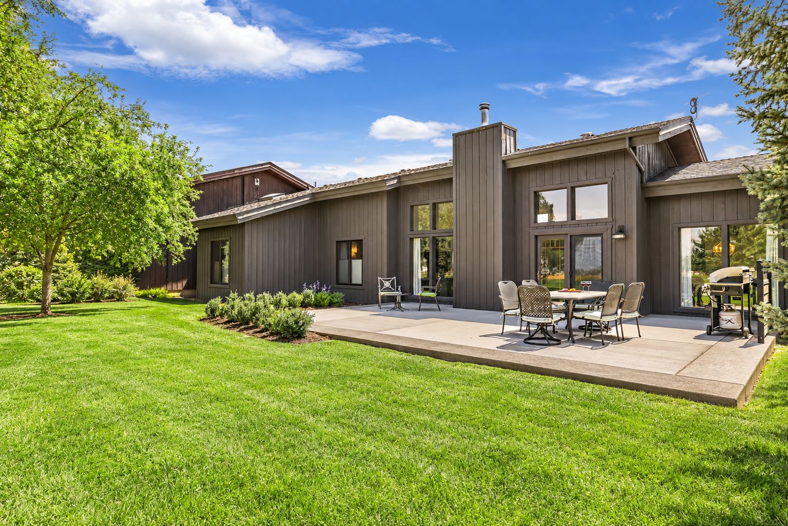 Una casa moderna con un patio, mobiliario exterior y un césped cuidado.