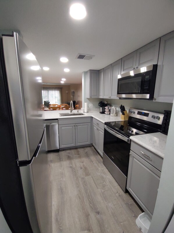 A modern kitchen with grey cabinets, a stainless steel refrigerator, a microwave, and an oven.