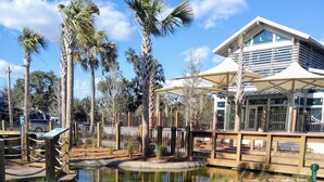 A view of a water feature with a wooden fence, palm trees, and a building with large windows in the background. - SOUTH FOREST BEACH. Coligny, pool. walk to beach. updated. sleep 8. 
SURF COURT (Hilton Head Island)