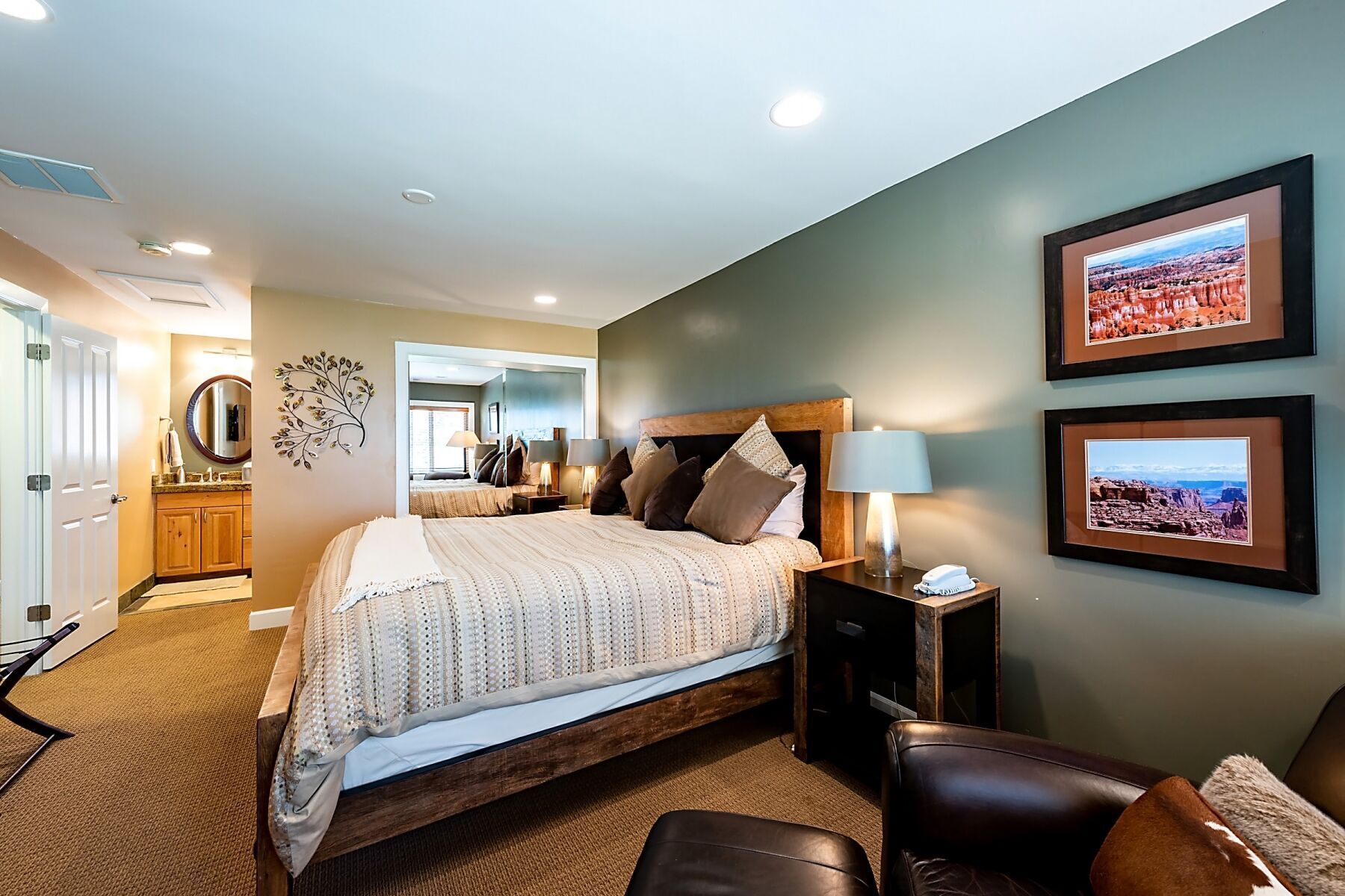 A bedroom with a large bed, bedside lamps, a wooden headboard, a nightstand, and two framed pictures on the wall.