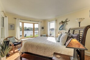 Quarto com cama grande, uma cadeira, uma mesa e vista para um lago.