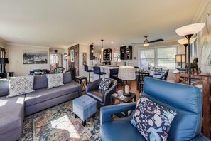 Uma sala de estar moderna com sofá, cadeiras, mesa de centro, tapete, lareira, área de cozinha e mesa de jantar.