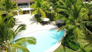 A pool surrounded by palm trees and a white building with a tiled roof. - WALKING DISTANCE TO THE BEACH (Casa de Campo)