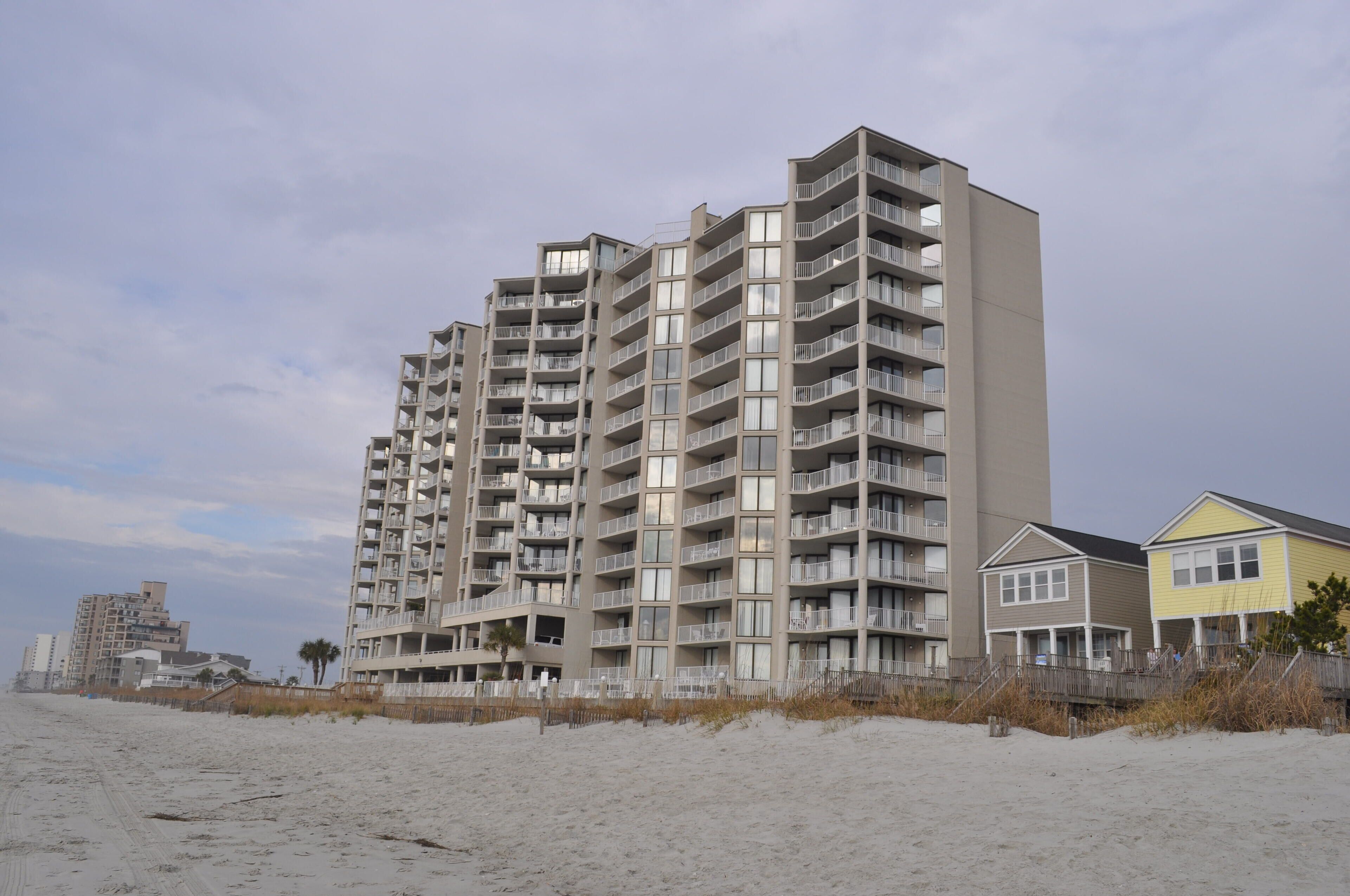 A multi-story hotel with balconies, located on a sandy beach.
