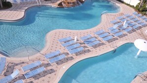 A large, curved swimming pool with clear blue water, surrounded by sun loungers and a tiled walkway.