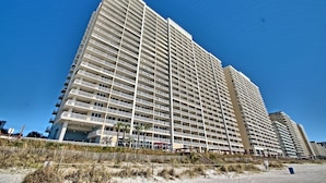 A high-rise hotel with multiple balconies, located near a beach.