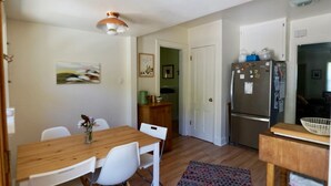 Een kleine keuken met een houten tafel, witte stoelen, een koelkast en een magnetron.