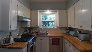 Een kleine keuken met witte kastjes, een kookplaat, een spoelbak en een raam met uitzicht op groen.