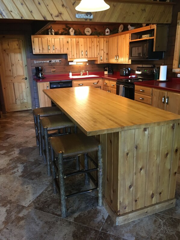 Una cocina de madera con una isla grande, taburetes de bar y una lámpara colgante.