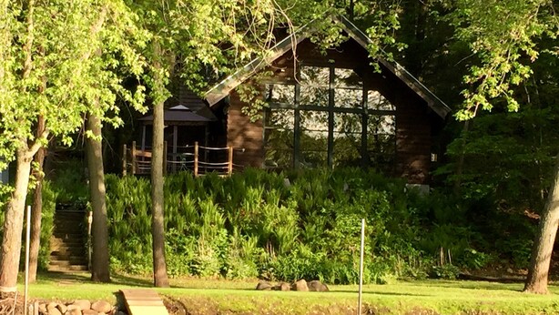 Une cabane en bois avec un quai s’avançant dans un lac paisible, entourée d’une végétation luxuriante et d’arbres.