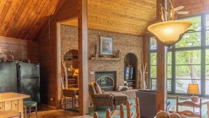 A rustic interior with a brick fireplace, wooden ceiling, and a dining area with a table and chairs.