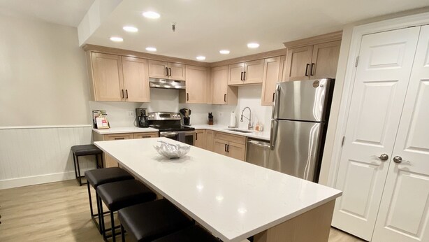 A modern kitchen with a central island, wooden cabinets, stainless steel appliances, and a white door. - Luxury Heart Of Old Town 3-Bdrm+ HOT TUB Walk To Skiing Chairlift Dining Main St (Park City)
