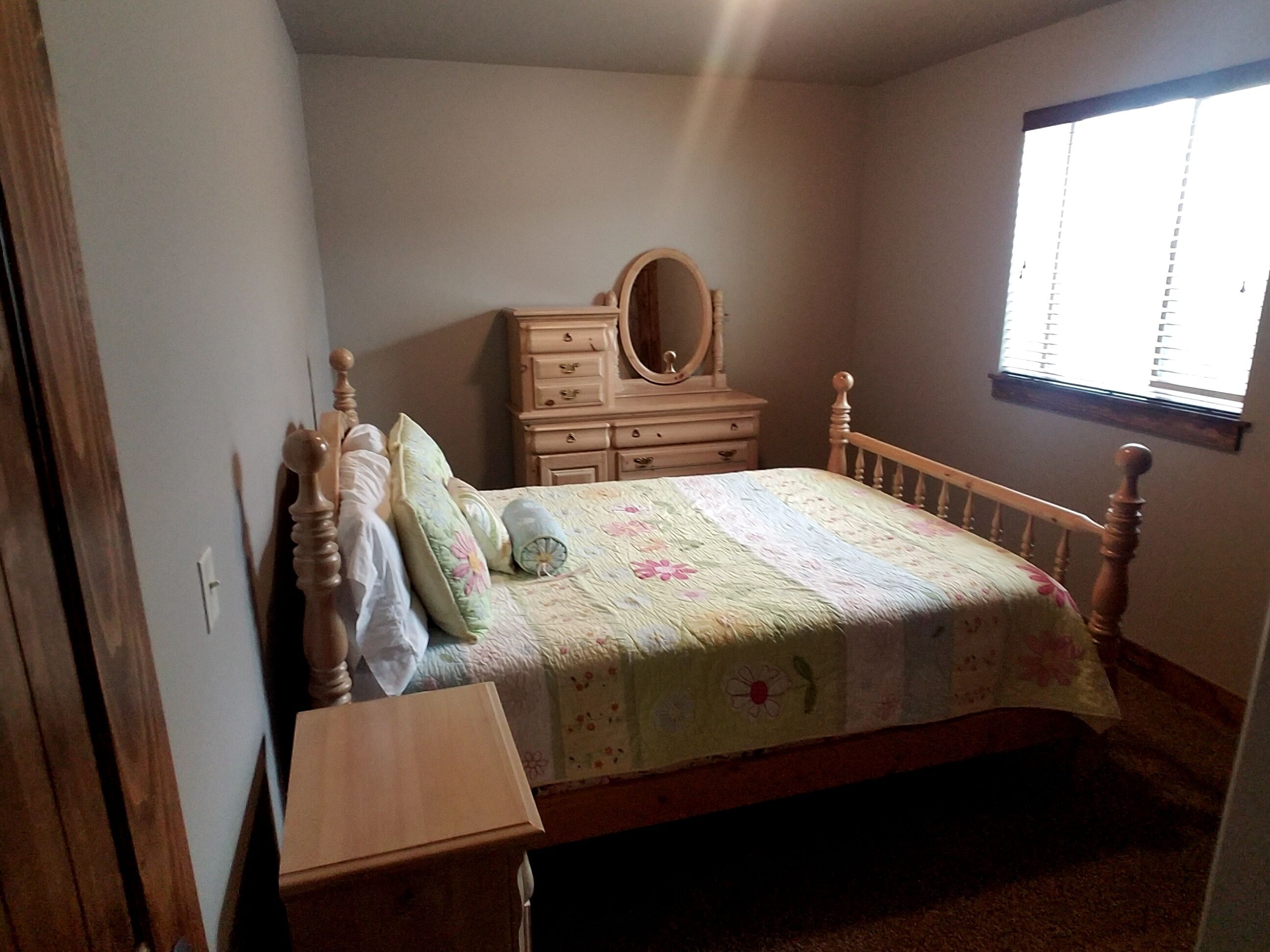 A bedroom with a wooden bed, a dresser, a mirror, and a window.