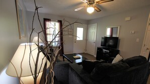 A living room with a sofa, a coffee table, a lamp, and a television. - Pet Friendly Condo Overlooking Pool And Tennis Court.  (Monticello)